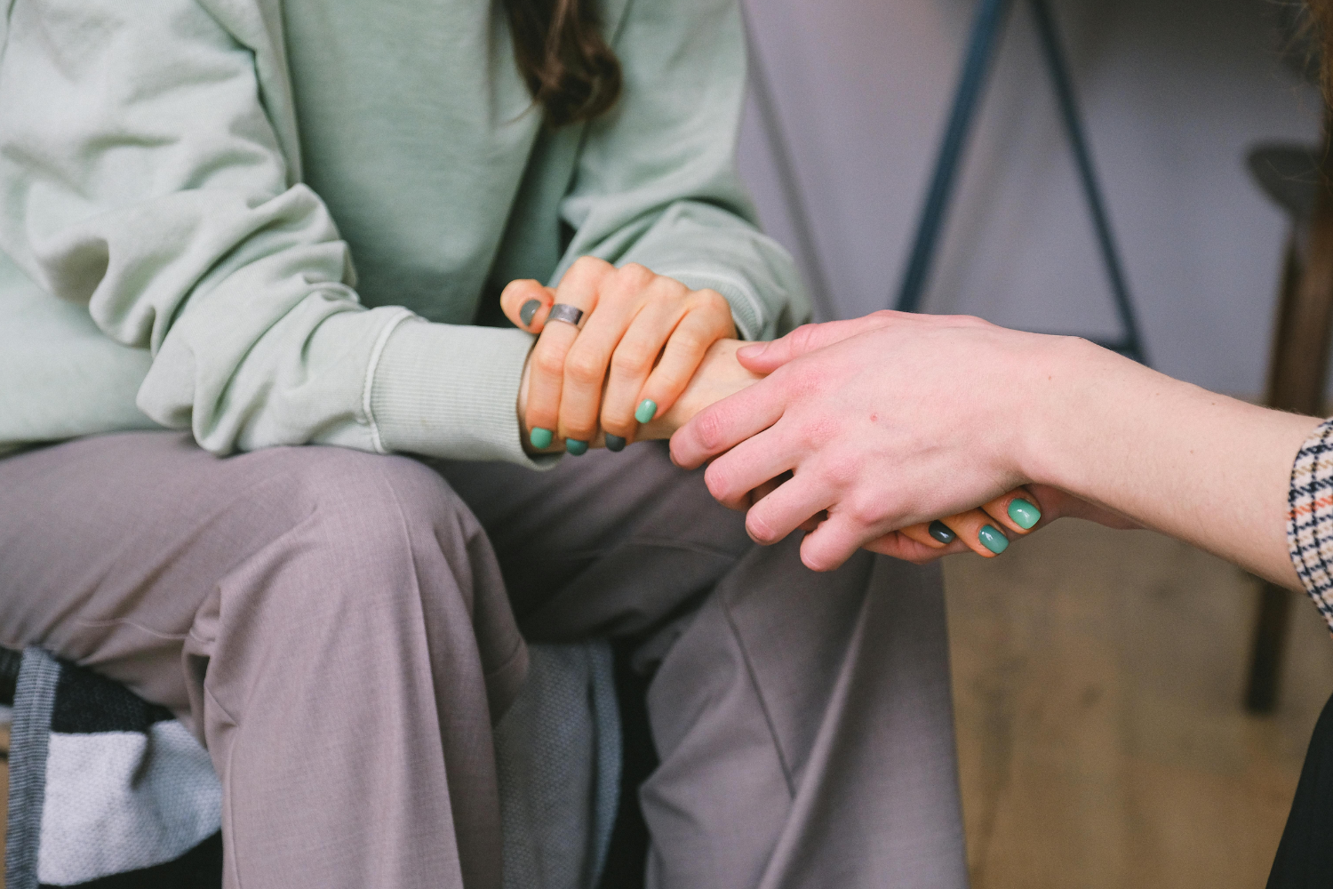 Two people hold hands, offering support and comfort in a close-up, indoor shot.
