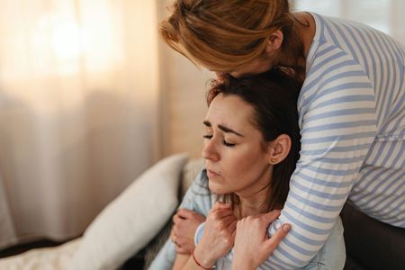 A person in a striped shirt comforts a distressed person who is leaning their head against them.