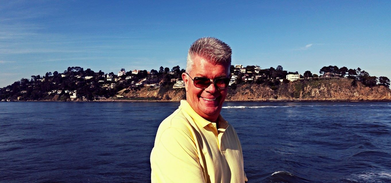 A man in a yellow shirt is standing in front of a body of water
