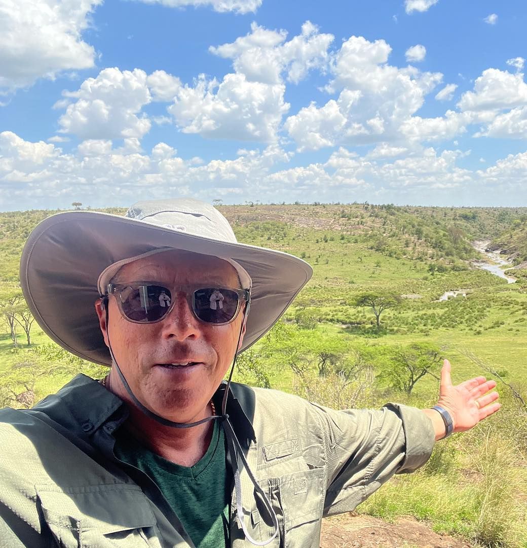A man wearing a hat and sunglasses is standing in a field.