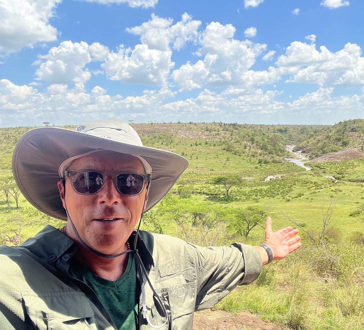 A man wearing a cowboy hat and sunglasses is standing in a field.