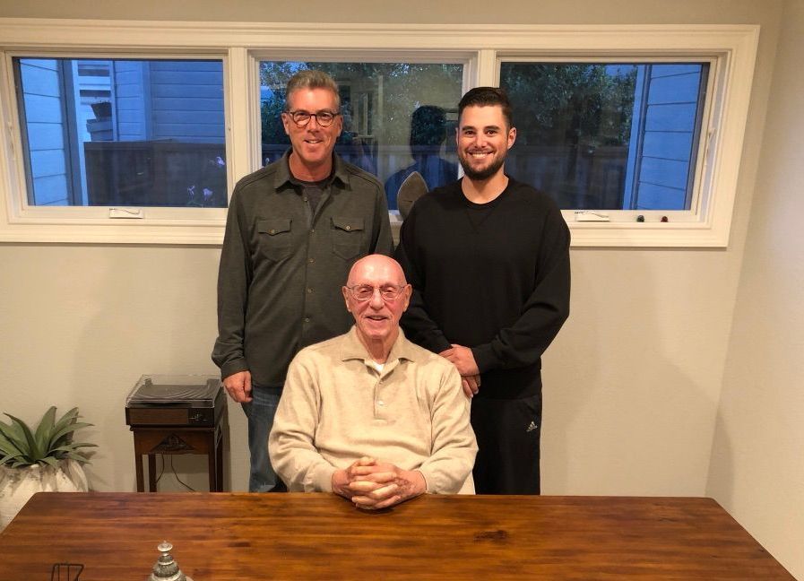 Three men are posing for a picture in a room with a man sitting at a table.