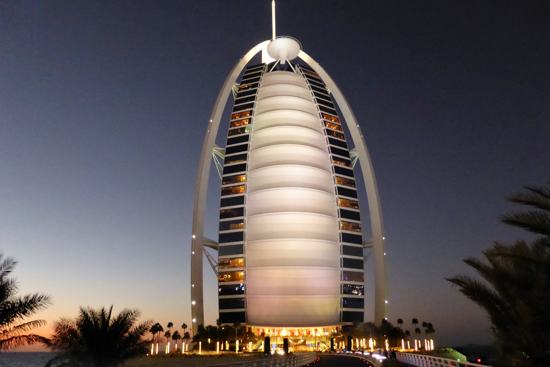 The burj khalifa is lit up at night with palm trees in the foreground