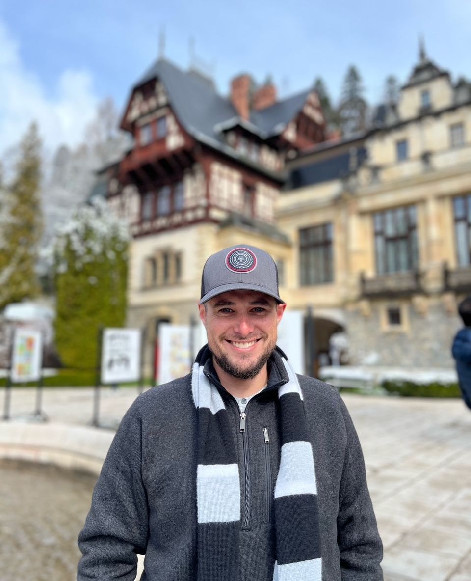 A man wearing a hat and scarf is standing in front of a building.