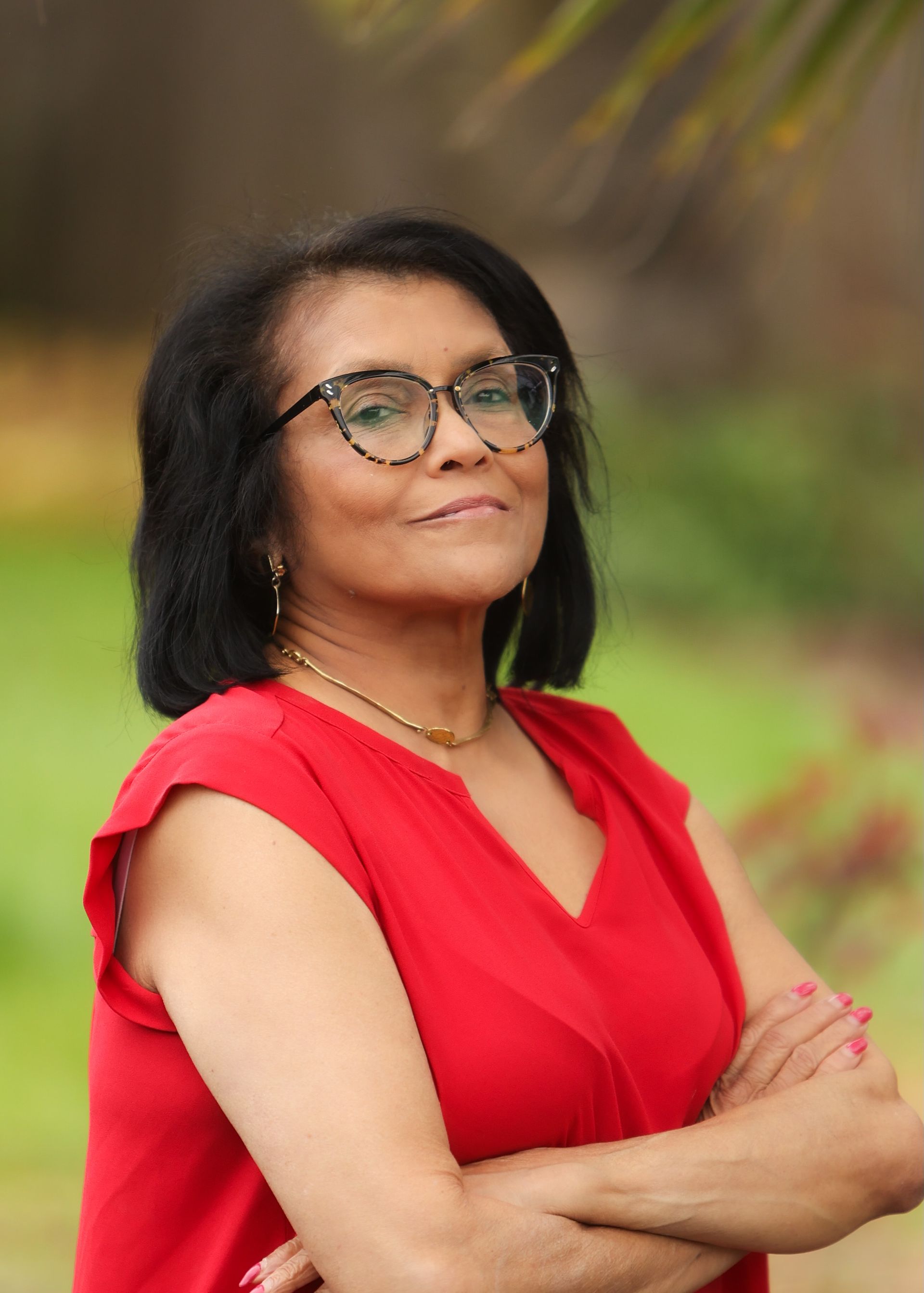 A woman wearing glasses and a red shirt is standing with her arms crossed.