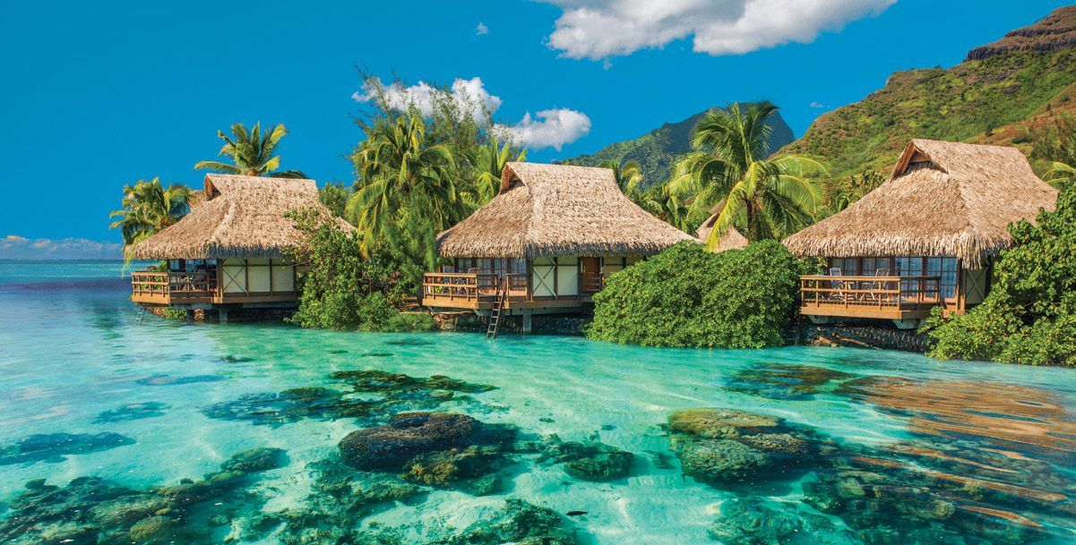 A row of thatched huts on a small island in the middle of the ocean.
