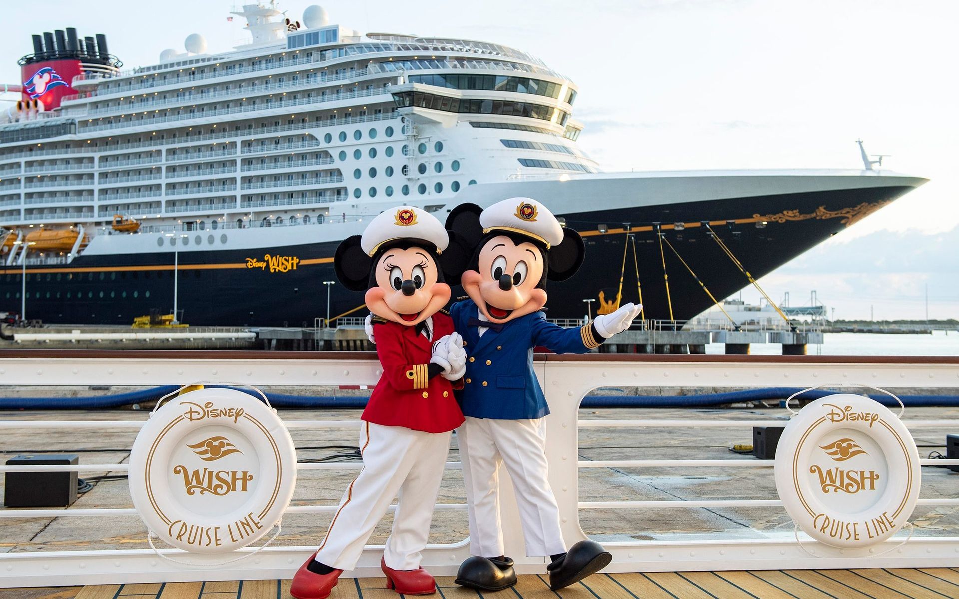 Two mickey mouse mascots are posing for a picture in front of a cruise ship