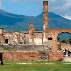 A group of people are standing in front of a ruined building with mountains in the background.