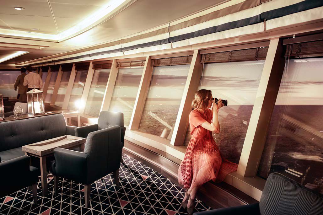 A woman in a red dress is taking a picture in a room with a lot of windows.