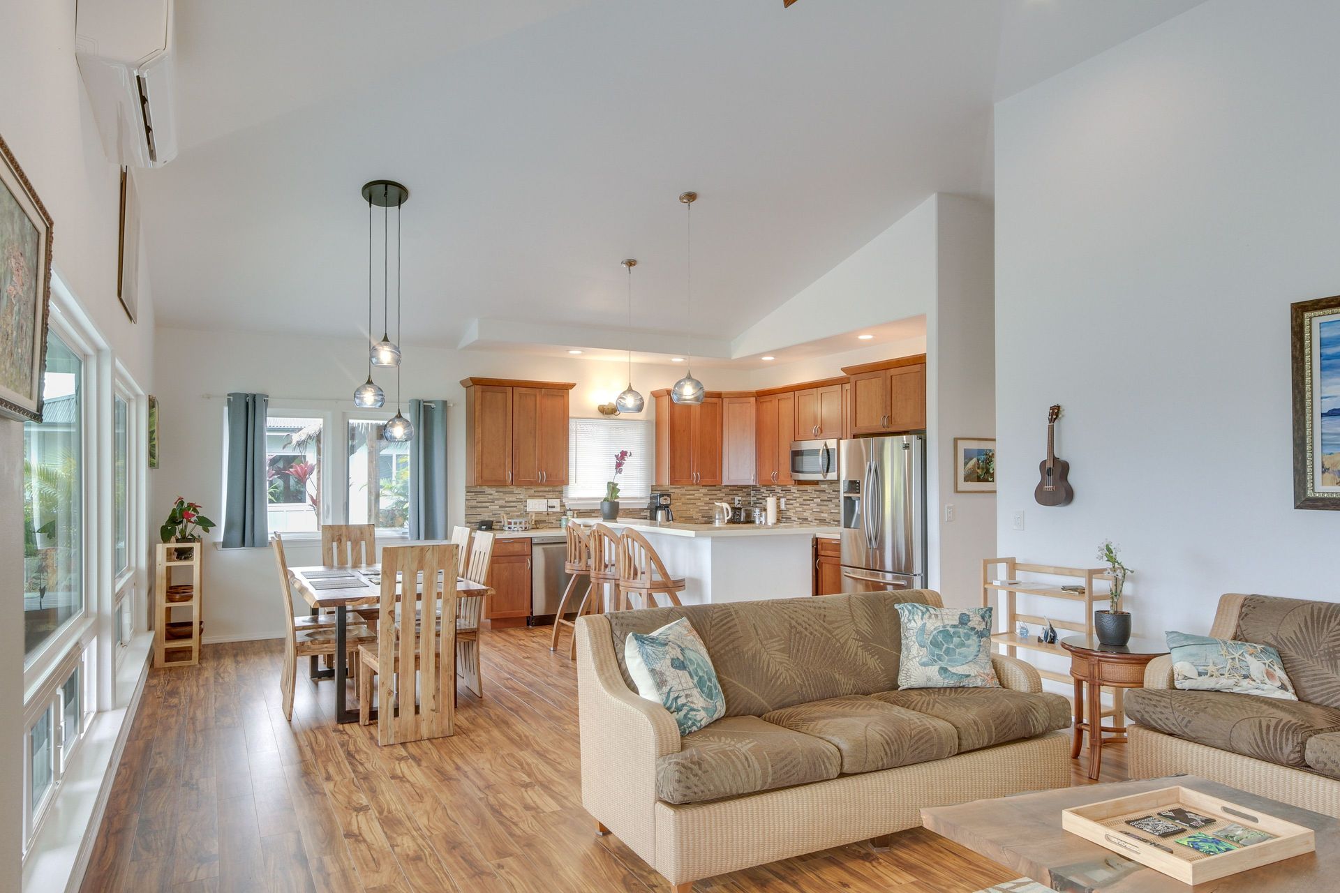 Hale Koholā: Open-concept living space with kitchen, dining area, and seating. Light wood floors, white walls, and brown furniture.