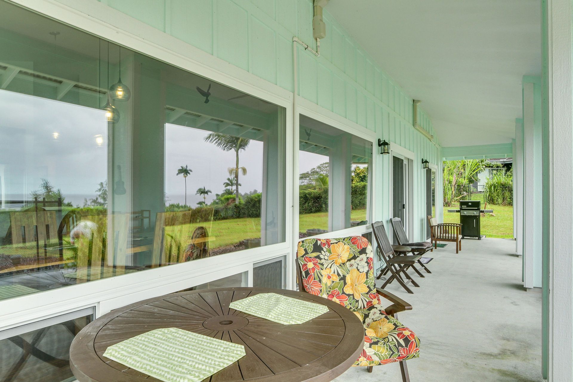Hale Koholā: Covered porch with table, chairs, and view of a grassy yard with trees.