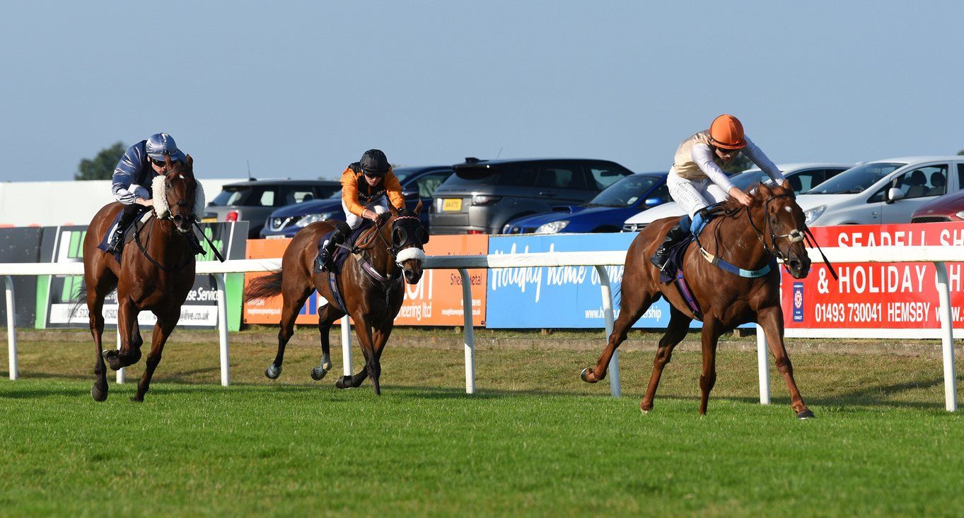 Three horses are racing on a track with a sign in the background that says holiday