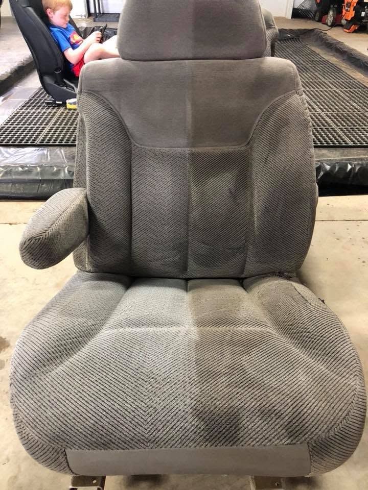 Gray padded car seat with armrests in a vehicle interior; child visible in the background.