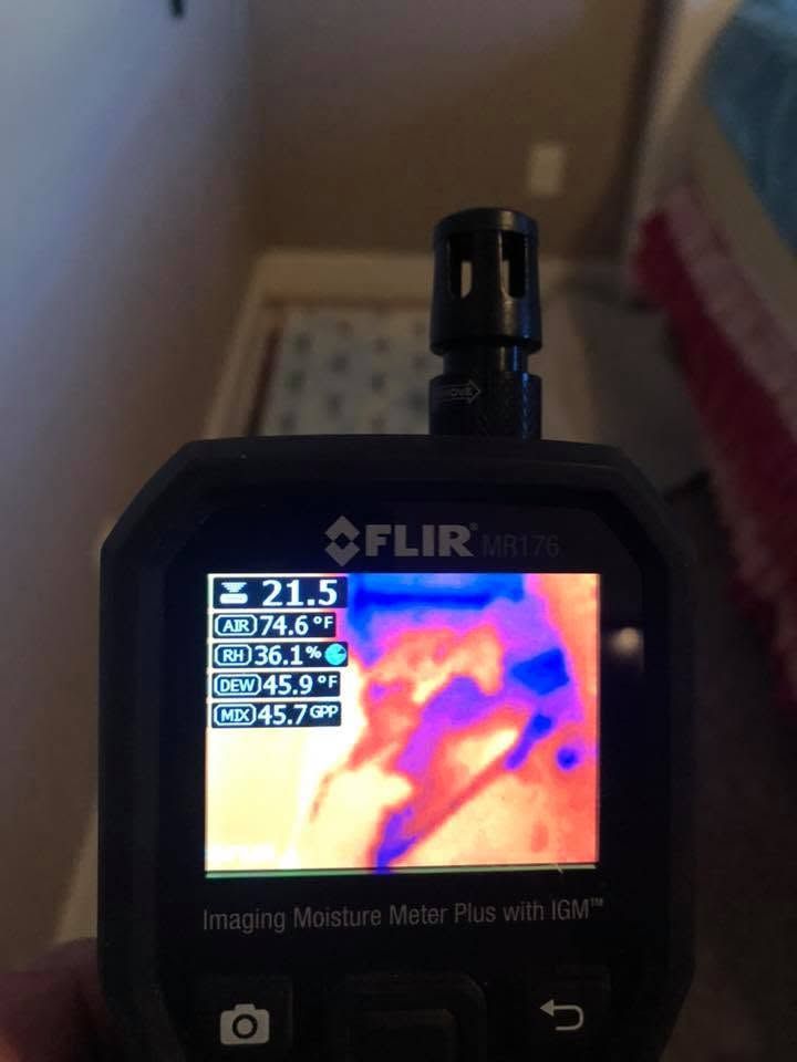 Handheld FLIR thermal camera displaying a colorful heat map on its screen indoors