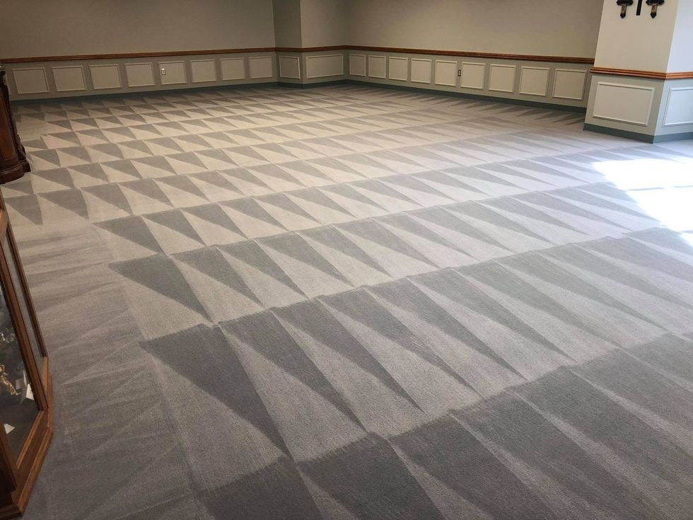 Empty carpeted room with patterned gray floor, beige walls, and sunlight from the right side.