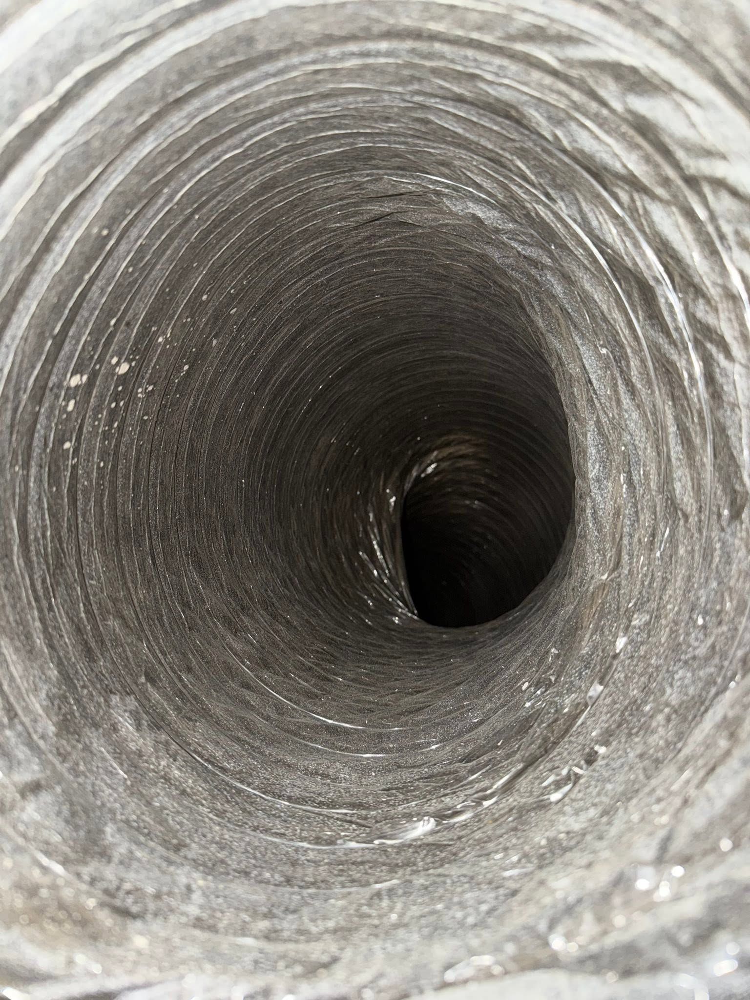 Looking down a narrow gray concrete tunnel or pipe with a dark opening at the far end