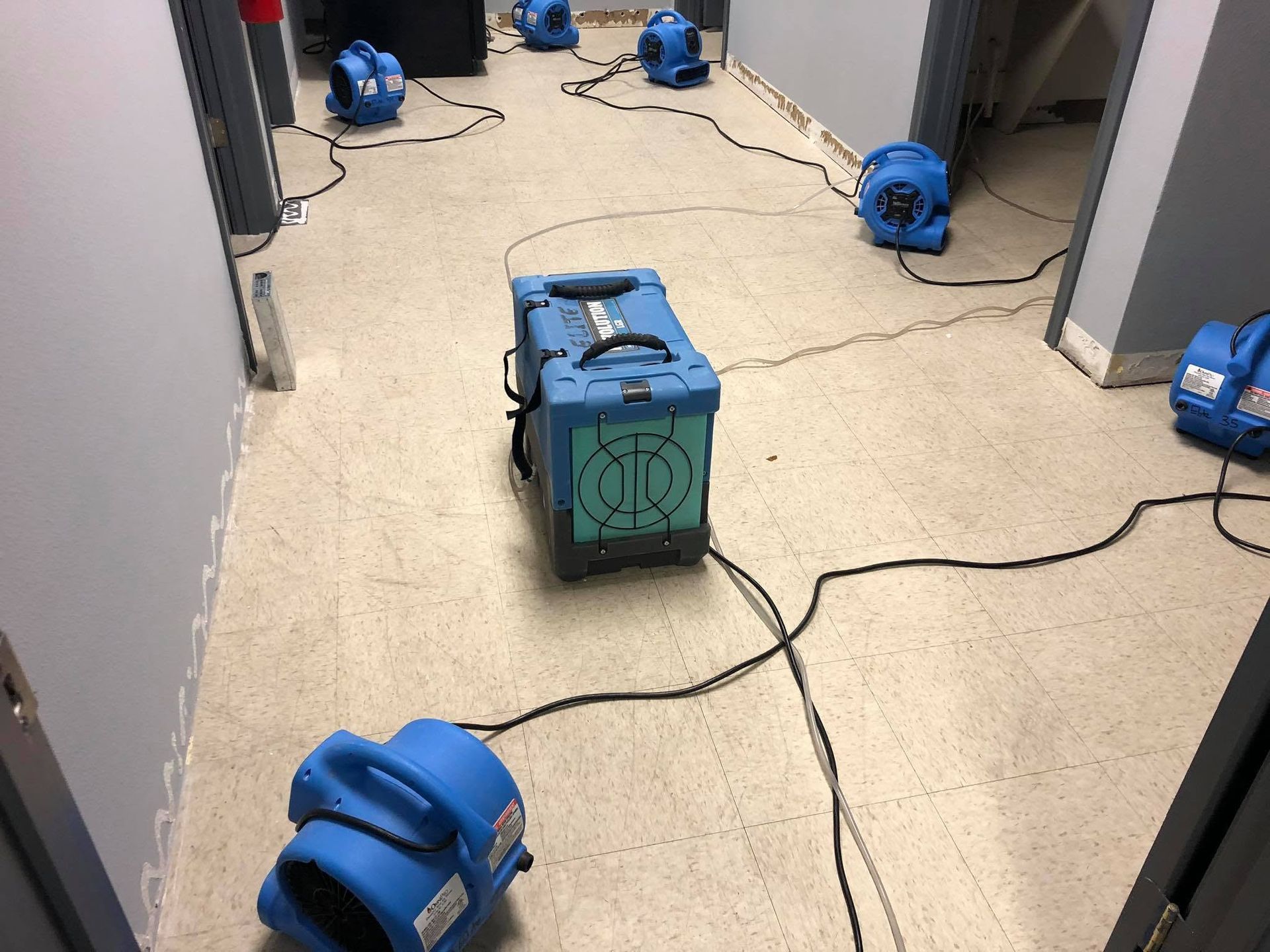 Blue equipment on a hallway floor with tangled cables and a green box in the center.