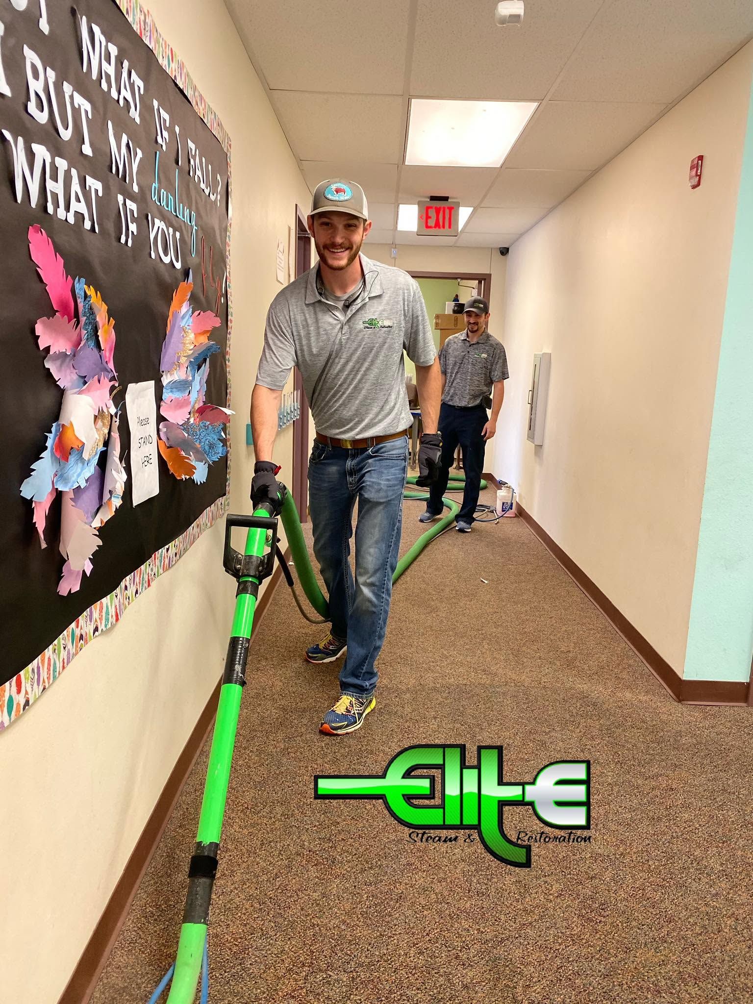 Two people walking down a school hallway with a green barrier on the floor