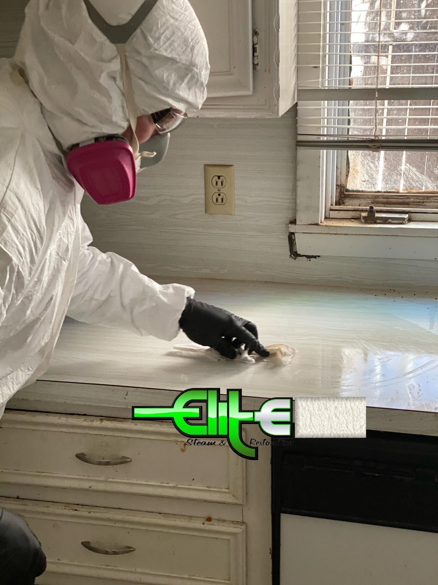 Person in protective suit and respirator cleaning a kitchen counter with a spray bottle and cloth