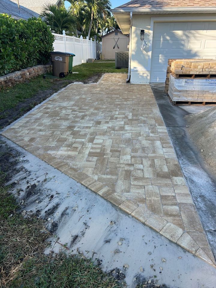 Paved driveway beside a garage, with a sidewalk leading to a yard and trash bin.