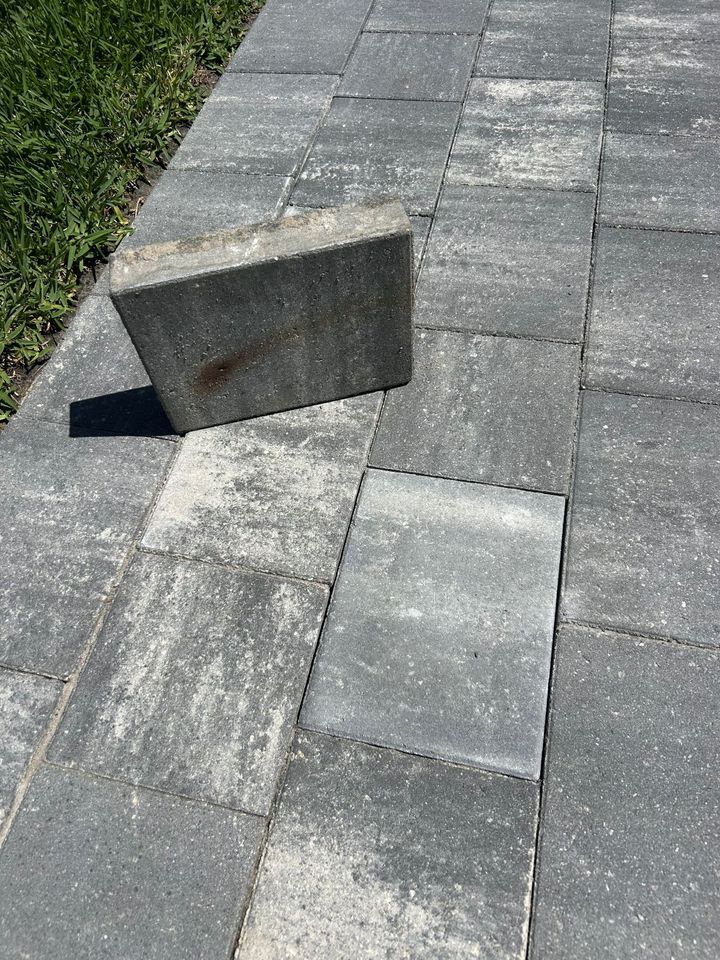 Concrete block resting on gray pavers beside grass, casting a shadow.