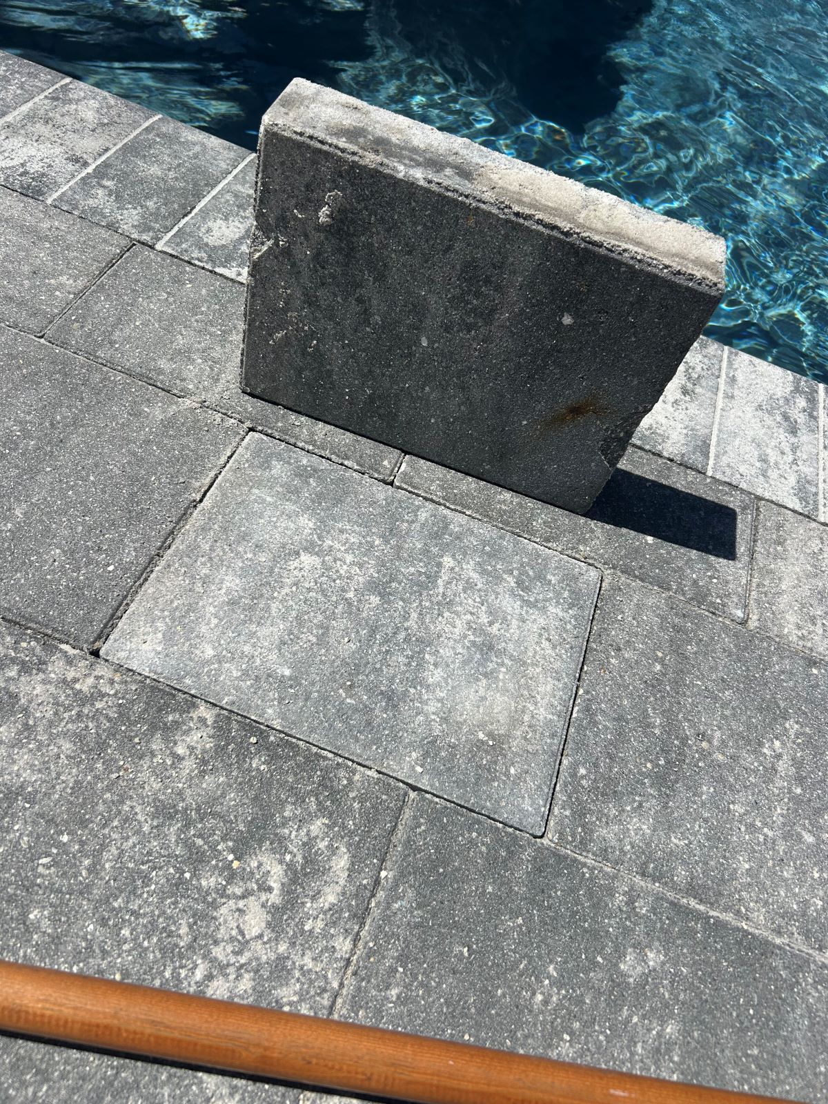 Stone dock edge beside blue water with a concrete block and a brown hose on gray pavement