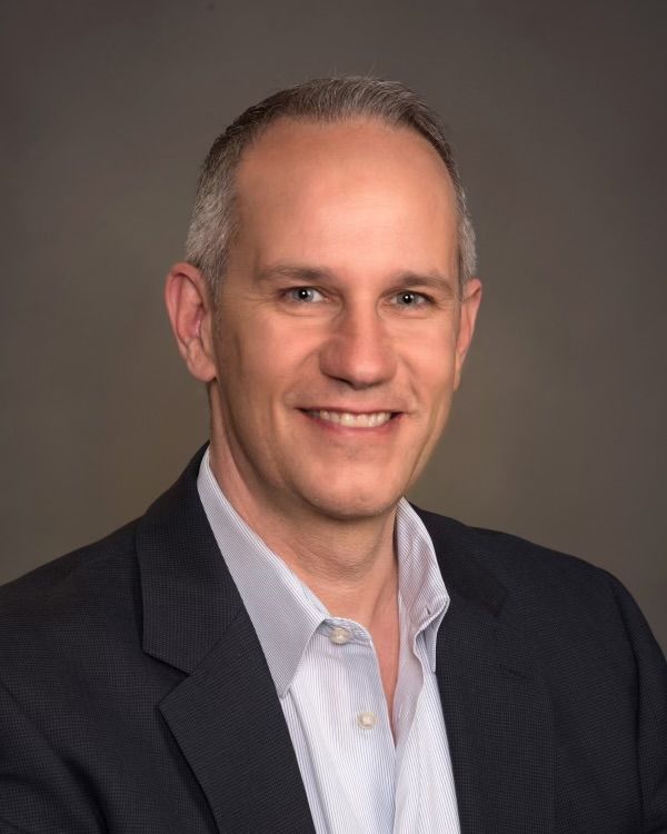 A man in a suit and white shirt is smiling for the camera.