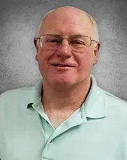A man wearing glasses and a light blue shirt is smiling for the camera.