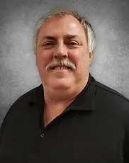 A man with a mustache is wearing a black shirt and smiling.