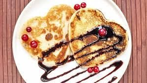 Two pancakes with chocolate sauce and cherries on a white plate.