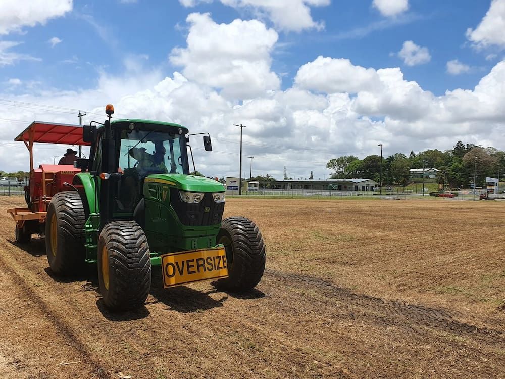 A Green Tractor Is Towing A Red Tractor In A Field — Marian Lawns In Marian, QLD