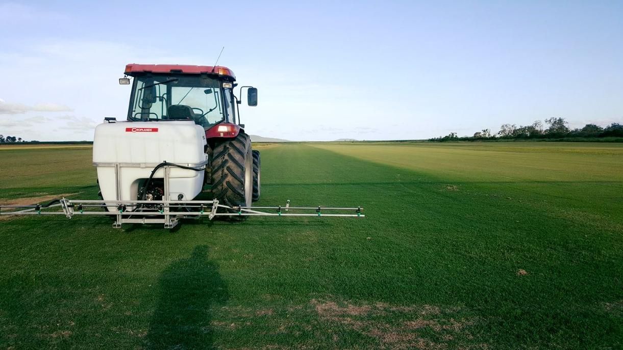 A Tractor Is Spraying Fertilizer On A Lush Green Field — Marian Lawns In Marian, QLD