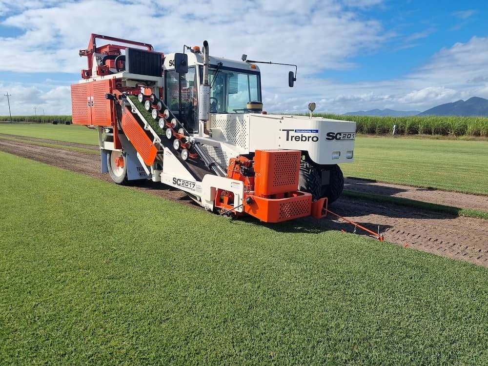 A White And Orange Tractor Is Parked In A Grassy Field — Marian Lawns In Marian, QLD