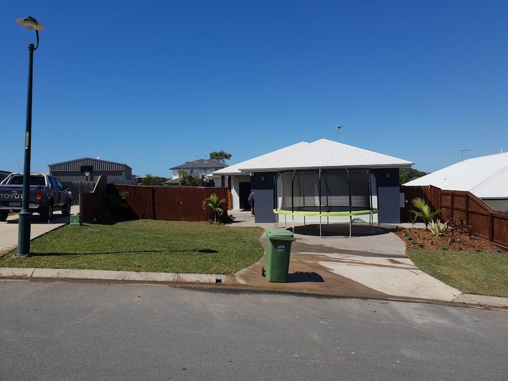 A White House With A Green Trash Can In Front Of It — Marian Lawns In Bowen, QLD