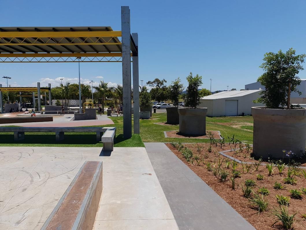 A Park With A Concrete Walkway And Planters With Trees In Them — Marian Lawns In Marian, QLD