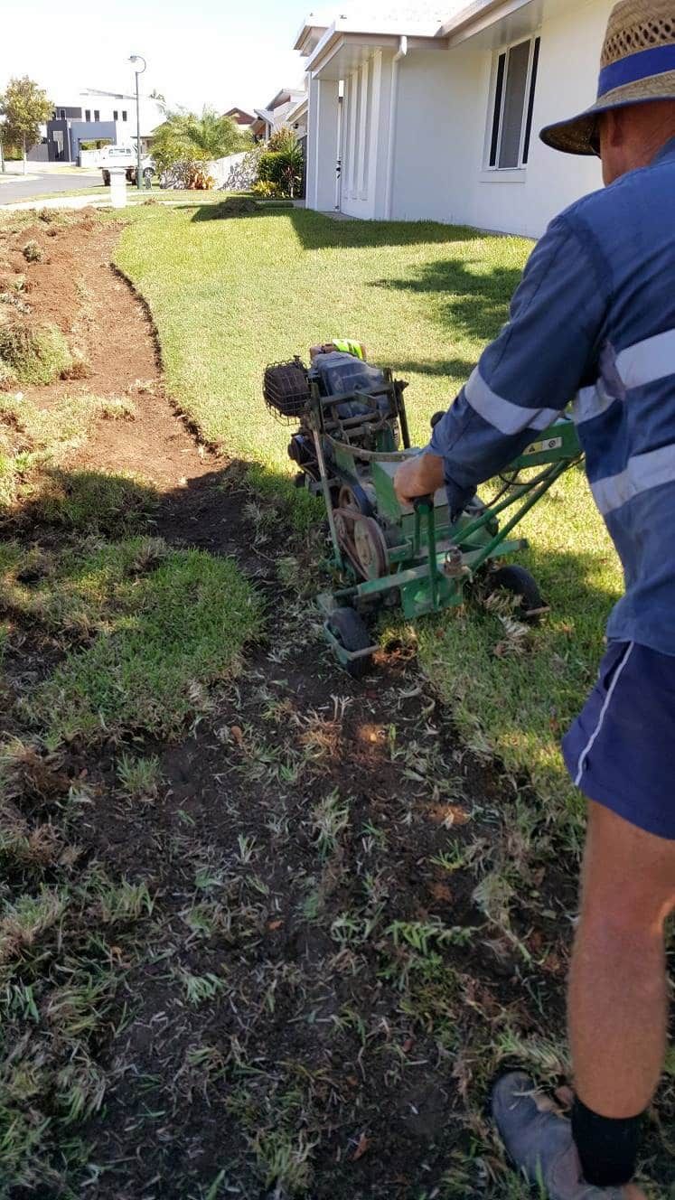 A Man Is Using A Machine To Remove Grass From A Yard — Marian Lawns In Sarina, QLD