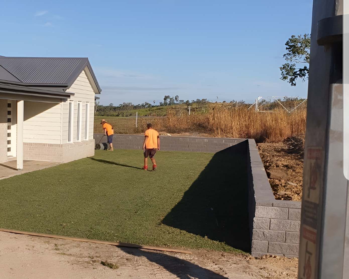 Two Men In Orange Shirts Are Standing In Front Of A House — Marian Lawns In Cannonvale, QLD