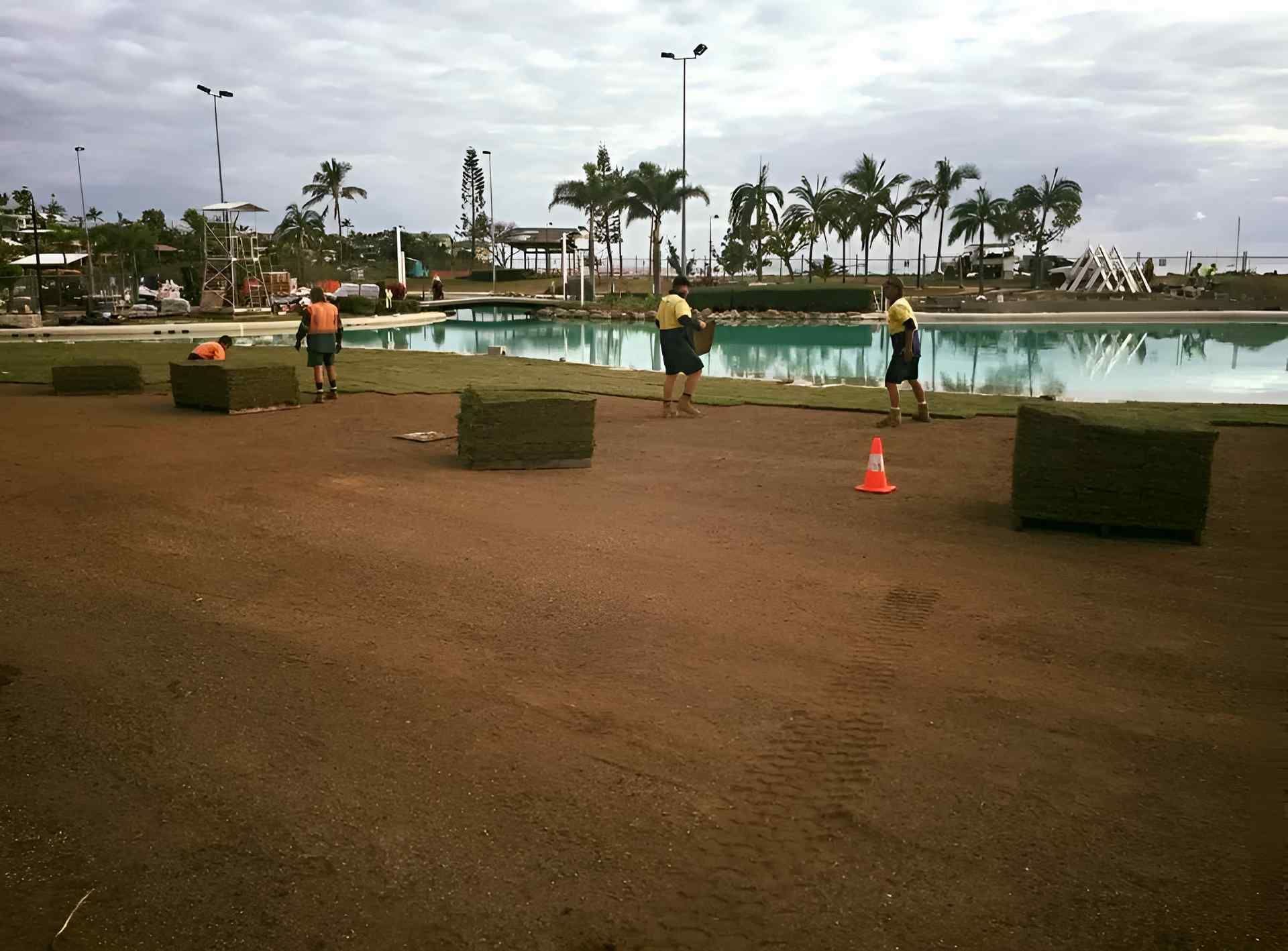 A Group Of People Are Working On A Lawn In Front Of A Pool — Marian Lawns In Sarina, QLD
