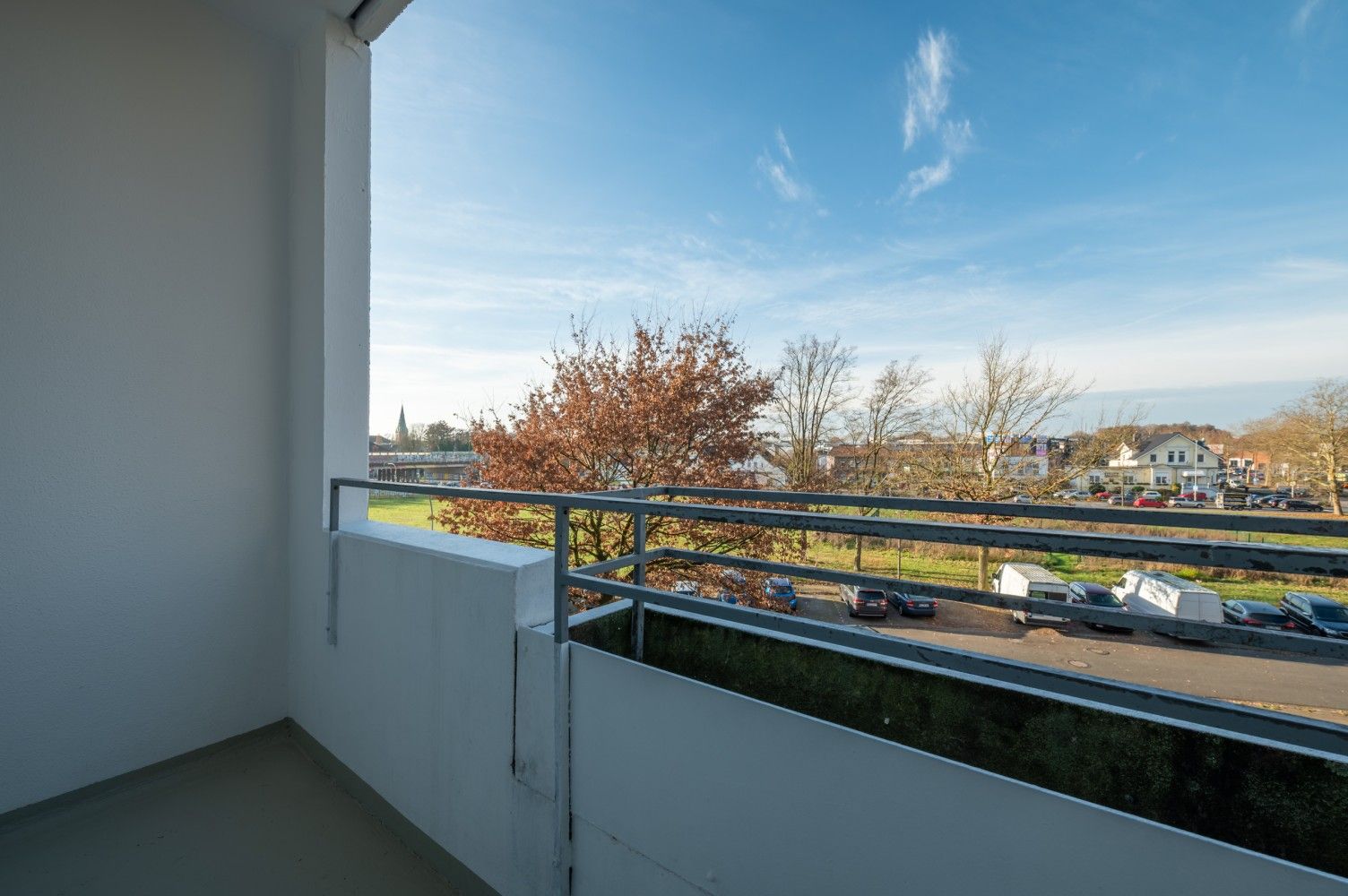 Ein leerer Balkon mit Blick auf Bäume, geparkte Autos und blauen Himmel an einem sonnigen Tag
