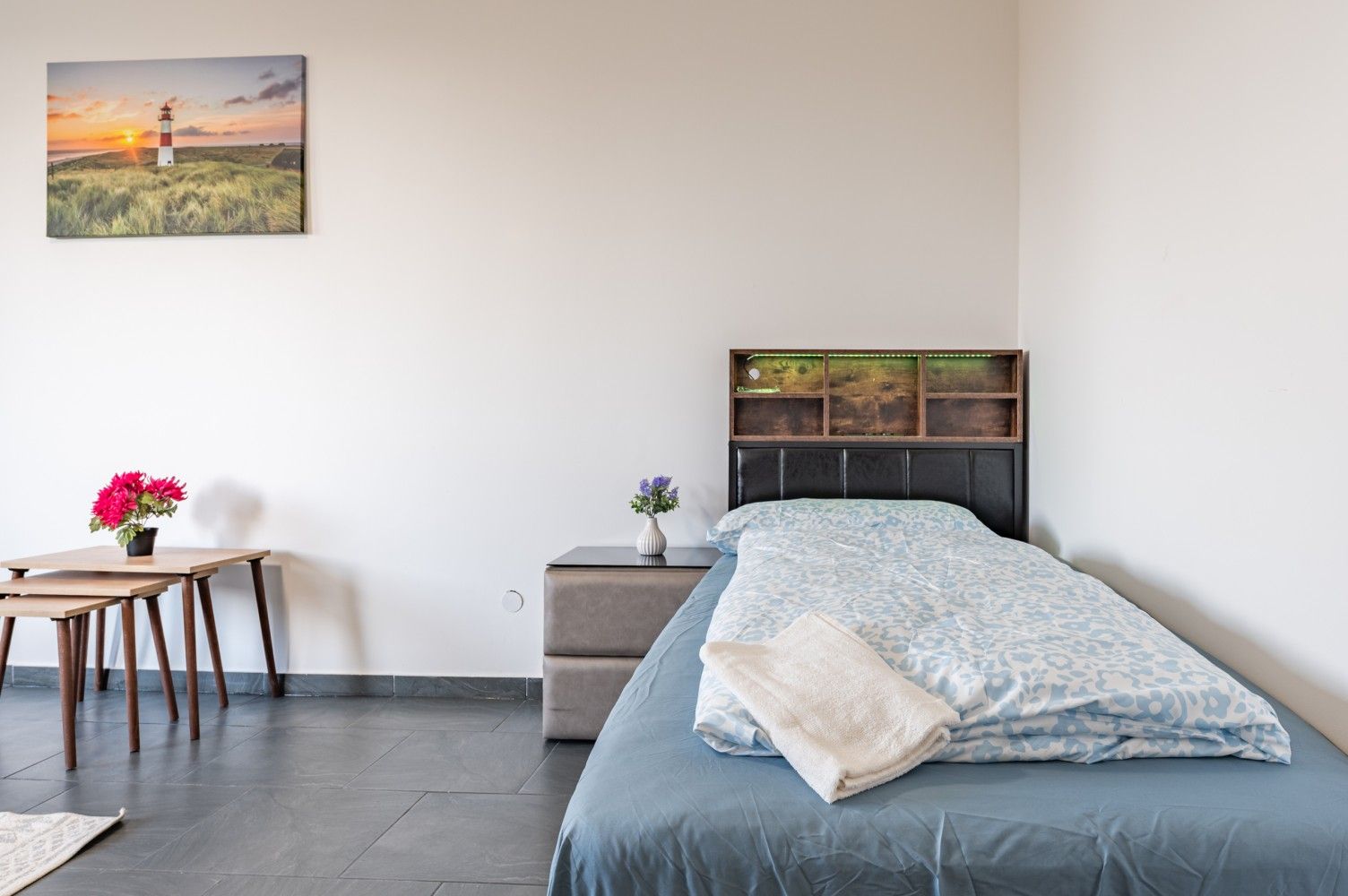 Minimalistisches Schlafzimmer mit Bett, Nachttisch, kleinem Schreibtisch und Wandbildern in einem hellen Raum