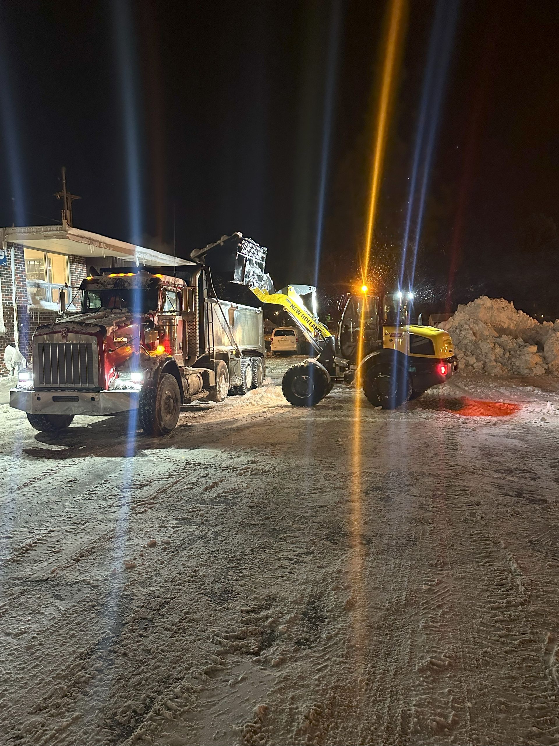 Night roadside emergency scene with a utility truck, worker, and excavator beside a snowy road
