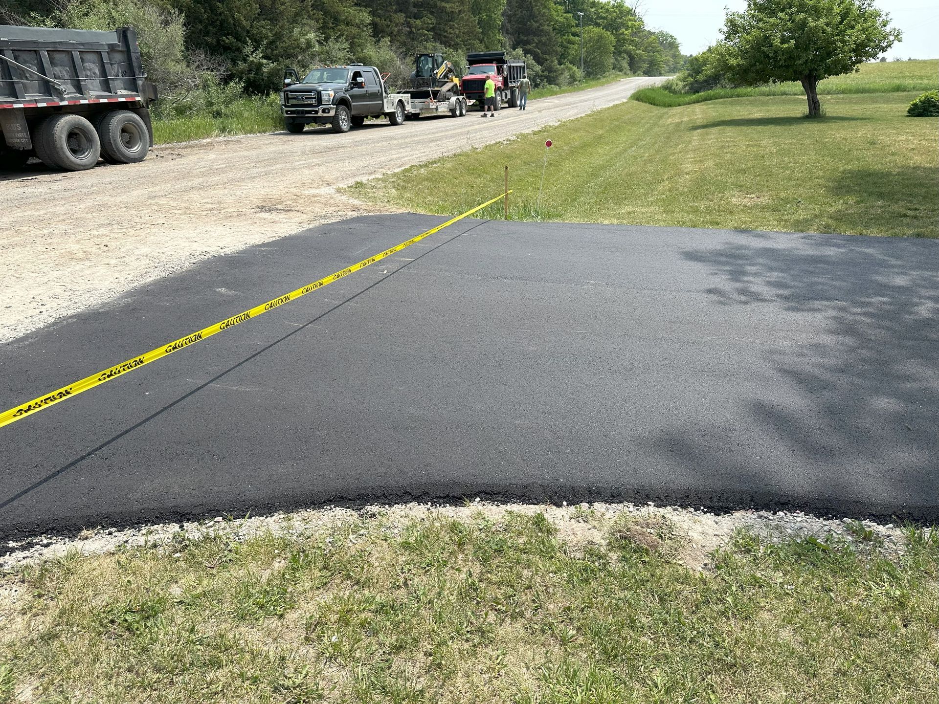 Fresh black asphalt patch beside a gravel road with construction vehicles in the background