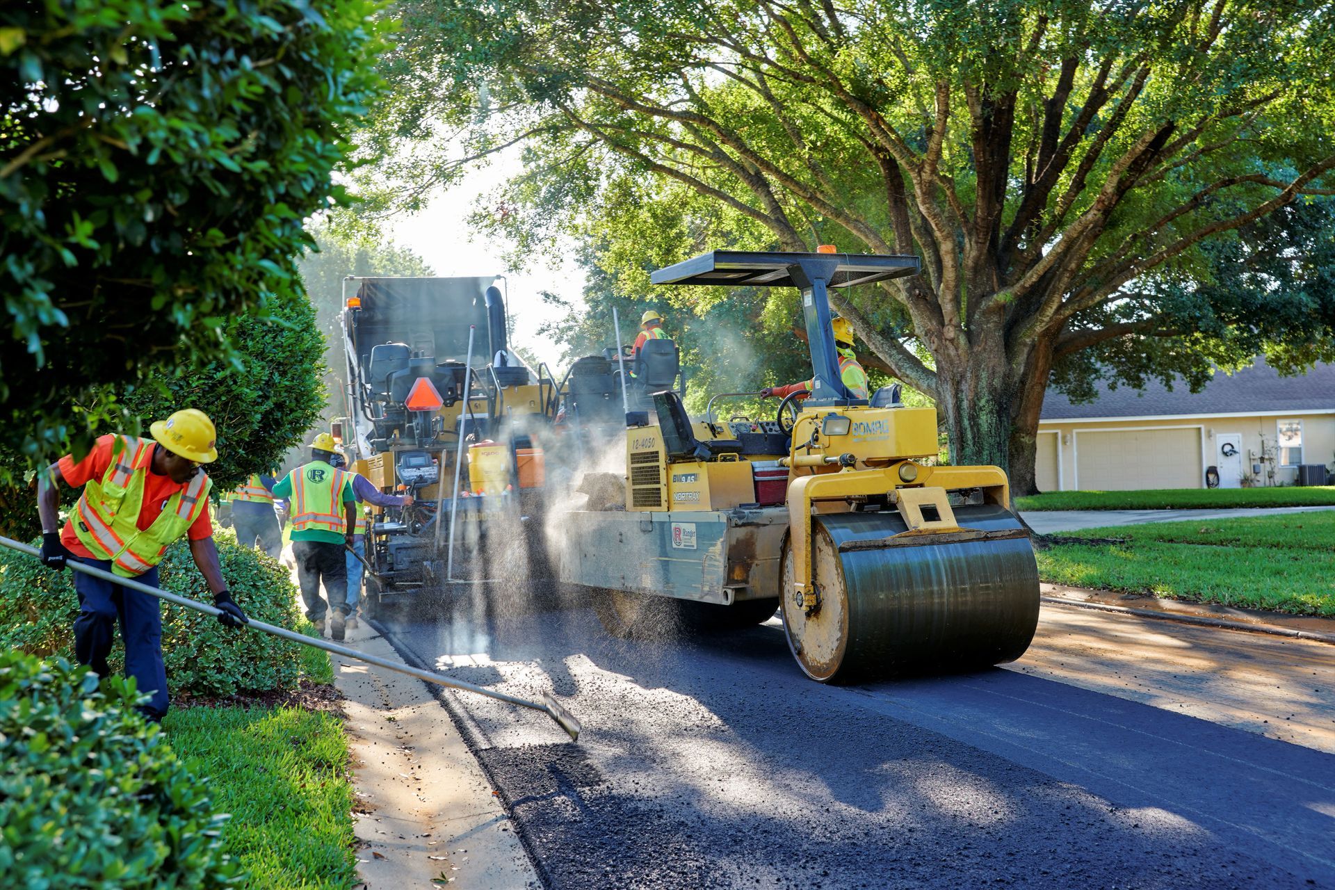 a man wearing a yellow hard hat is standing next to a road roller