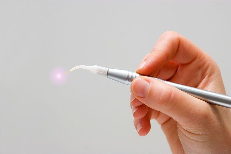 Hand holding a dental laser, emitting a pink beam.