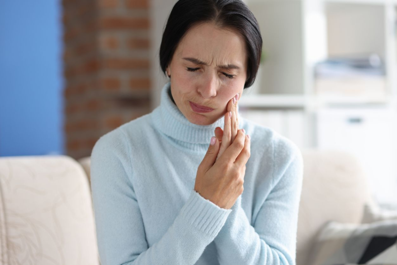 Woman with clenched jaw, holding cheek; appears to have a toothache.
