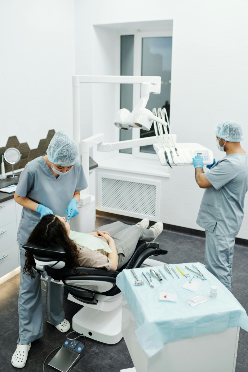 Dentist and assistant treating a patient in a dental clinic. They wear scrubs and the patient is in a dental chair.
