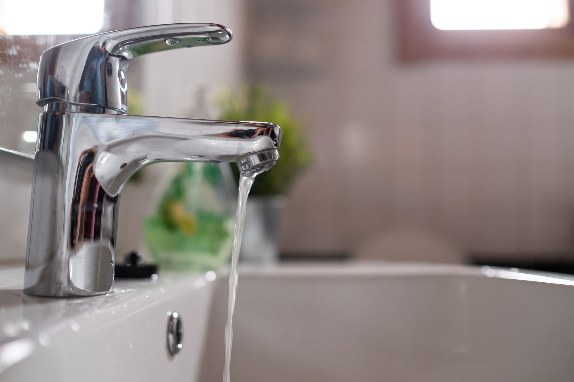 Water flowing from a chrome bathroom faucet into a white sink.