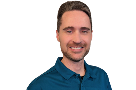 A man with short brown hair and a beard, smiling, wearing a dark teal polo shirt against a white background.