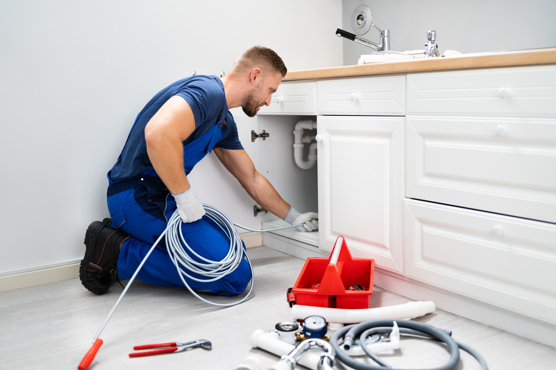 A plumber is cleaning a clogged sink pipe in the kitchen.