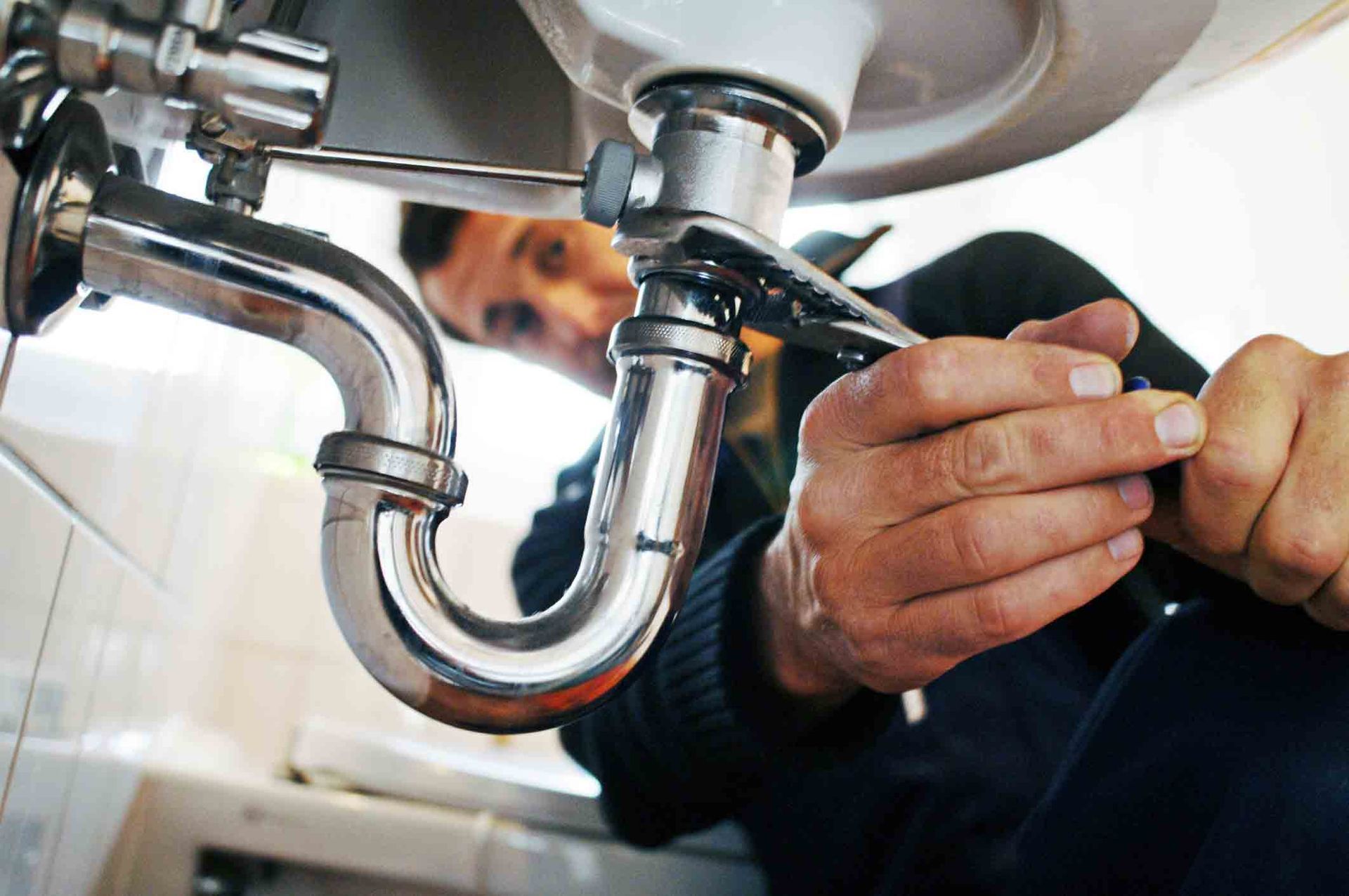 Close-up of a skilled plumber in Colorado Springs, using a wrench to repair a sink in a bathroom.